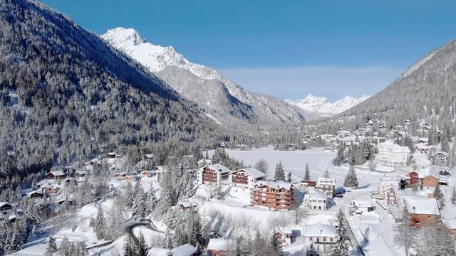 4K Winter holidays - lovely mountain ski resort with frozen lake on a sunny day. Cinematic drone shot and beautiful snowy panorama
