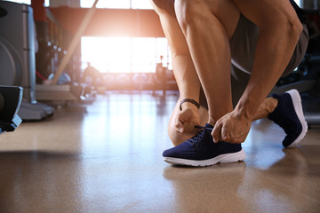 Obraz na płótnie Canvas Sporty young man tying shoelaces in gym