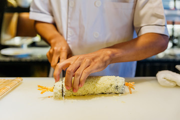 Chef cut a rolling Maki Sushi with Rice, Shrimp Tempura, Avocado and Cheese inside covered Crispy Tempura Flour.