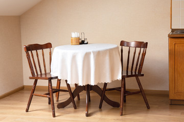 Small table with white cloth on it and two chairs in the corner of the room