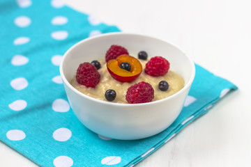 Healthy breakfast porridge for kids. Bowl of baby food on a fabric on white wooden background. The concept of proper nutrition and healthy food.