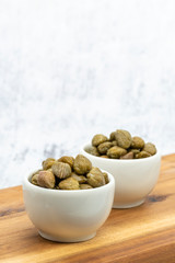 Green pickled capers in a white bowl on a wooden table, closeup. Mediterranean food.