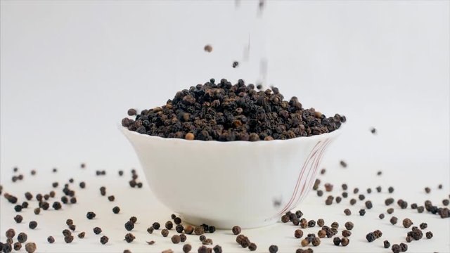 Shot of falling peppercorns / black pepper/kali mirch in a white bowl - Indian flavor. 