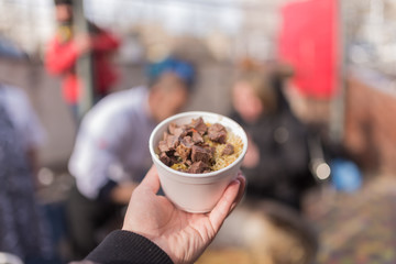 Hand holds bowl with meat and rice.