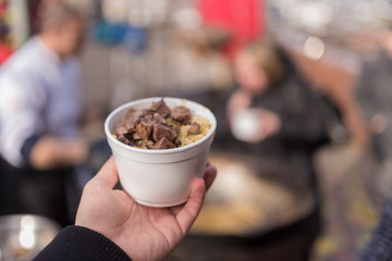 Hand holds bowl with meat and rice.