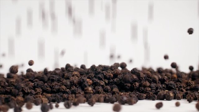 Shot of black pepper (Kaali Mirch - Indian Spice) is falling on a white table. 