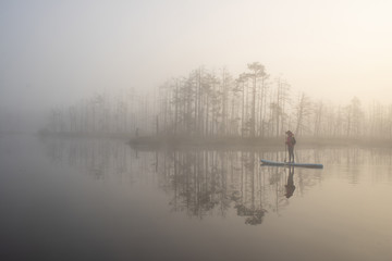 Woman slowly floating on the water on the sup-board. Fog and swamp.