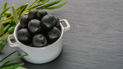Bowl filled with freshly harvested whole black olives near branches with leaves and olives on a grey stone background with copy space for your text. Natural background. ECO products.