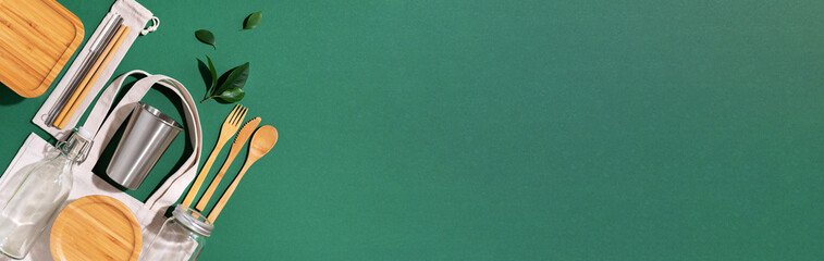 Sustainable lifestyle. Zero waste, plastic free shopping concept. Cotton bags, glass jar, bottle, metal cup, straws for drinking, bamboo cutlery and boxes on green background. Banner