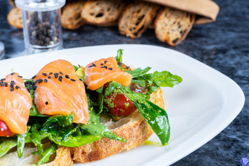 Close up view on delicious italian bruschetta with salmon, lettuce, cherry tomato and sauce on marble table. Italian cuisine. Top view with copy space. Flat lay food. Selective focus