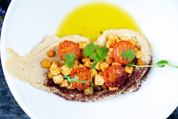 Close up view on hummus with halumi cheese, microgreen and tomato. Great israel cuisine appetizer in white plate. Vegan food. Top view