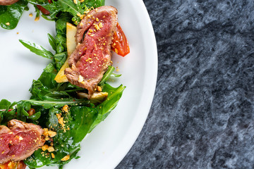 Close up view on Japanese cuisine styled salad Tataki with beaf (veal) spinach, arugula. Beef Tataki. Restaurant food for lunch. Flat lay food on marble table. Top view food photography