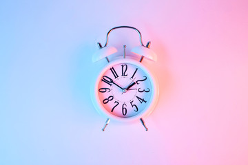 White antique alarm clock on in vibrant bold gradient purple and blue holographic colors. Concept art. Minimal summer surrealism.. Flat lay composition. Top view.	