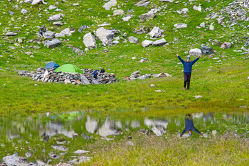 Happy young man near his tent in rocky mountains