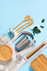 Cotton bags, glass jar, bottle, metal cup, straws for drinking, bamboo cutlery and boxes on blue background. Sustainable lifestyle. Zero waste, plastic free shopping concept
