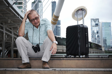 Asian Elderly tourist is sitting put his hand on head and depressed at the stairway of the sky train station due to wallet and passport stolen.