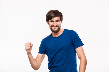 Young bearded brunet bearded man with mustaches in a blue shirt posing expressing gesture of victory with his arms standing isolated over white background. Concept of success.