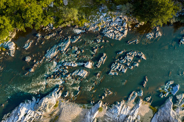 Aerial top-down photo of a river in a mountain canyon with green forest and rocks in the river