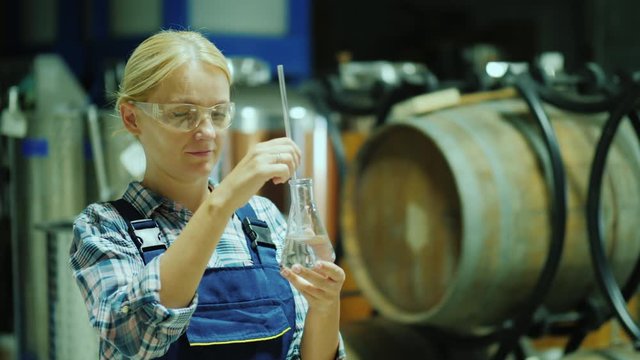 Female researcher working with product samples in a flask. Against the background of wooden barrels of wine