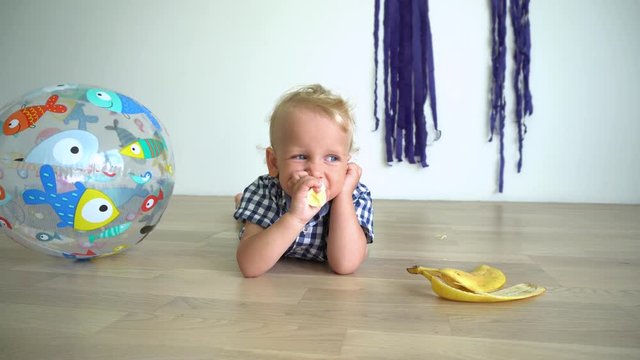 Careless toddler boy lying on floor and eating yellow banana. Gimbal motion