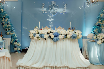 Wedding presidium in restaurant, free space. Luxury wedding decorations. Banquet table for newlyweds with flowers, greenery, blue cloth and candles. Lush floral arrangement. 
