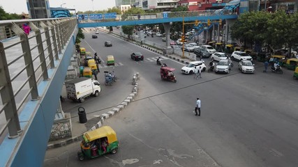 Time-lapse top view looking down at busy road intersection with vehicular traffic movement next to a modern CBD and commercial hub with a metro line  in national capital of Delhi, India