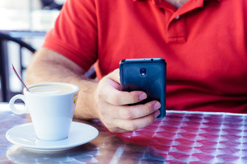 Man using a cell phone on cafe terrace and drink coffee
