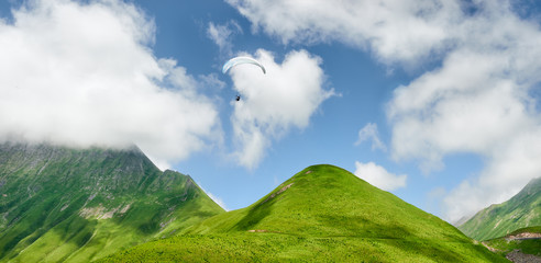 beautiful panoramic view of green hills and a flying paraglider against a blue sky and clouds