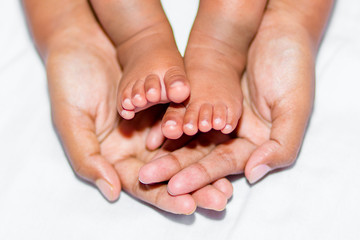 The soft legs of a baby placed on the palm of the mother's two hands on a white background.