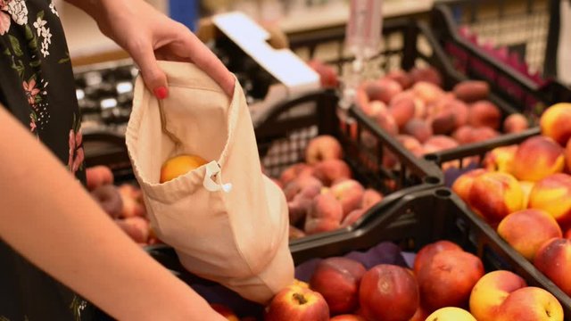 Woman in a supermarket takes fresh fruits to cotton bag. No plastic alternative. zero waste