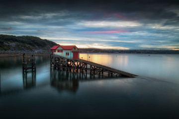Sunset and a calm evening tide at the old lifeboat station on Mumbles Pier, Swansea Bay, South Wales, UK