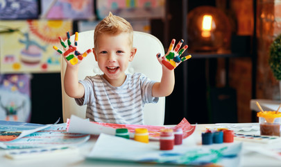 funny child boy draws laughing shows hands dirty with paint.