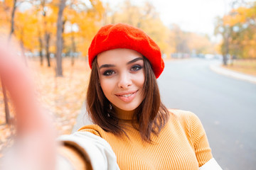 Portrait of cheerful young woman with autumn leafs in front of foliage making selfie.Portrait of...