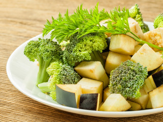 Sliced broccoli cabbage lies on a plate with pieces of eggplant on the table