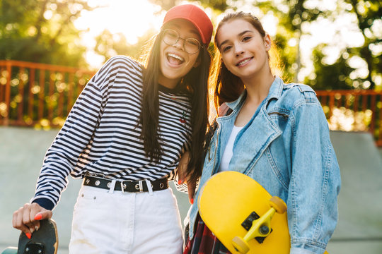 Image of two cute girls smiling and poising with skateboards in skate park