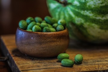 Still Life of a Large Watermelon on a Wooden Board next to a small wooden bowl of Mexican Sour Gherkins, selective focus on foreground