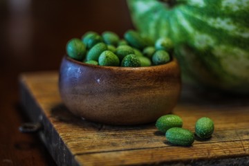 Still Life of a Large Watermelon on a Wooden Board next to a small wooden bowl of Mexican Sour Gherkins, selective focus on foreground