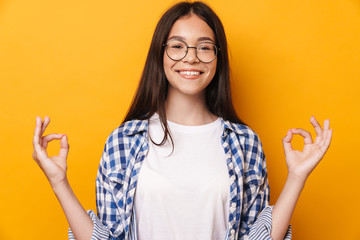 Pleased optimistic young cute teenage girl in glasses meditate isolated over yellow wall background.