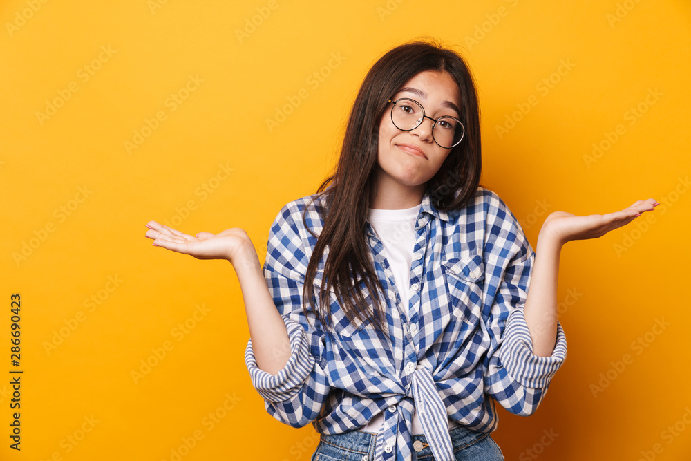 Sticker confused unsured young cute teenage girl in glasses posing isolated over yellow wall background.