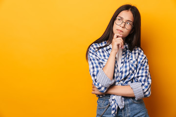 Fototapeta Thoughtful serious young cute teenage girl in glasses posing isolated over yellow wall background. obraz