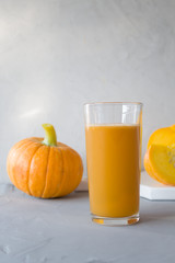 Fresh pumpkin juice in a glass glass, two pumpkins in the background on a gray background. The concept of proper, healthy eating. Autumn harvest. Vertical orientation, copy space.