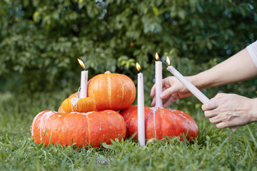 hands set fire and place holiday candles on orange halloween pumpkins in the park on a background of trees