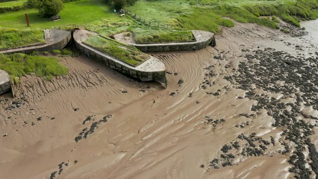 Aerial drone flight along abandoned shipwreck hulks on the side of a muddy river (Purton Hulks, England)