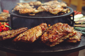 The chef is cooking meat on the grill. Golden rib steaks and chicken with grilled vegetables, delicious food