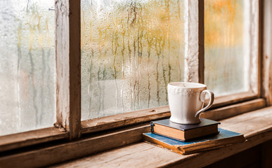 A white Cup and old books on the background of a rustic wooden wet window