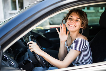 Fototapeta na wymiar Hello. Beautiful young cheerful women looking at camera with smile and waving while sitting in her car