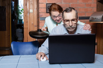 Family problems due to computer. Elderly couple in the kitchen, senior man uses a laptop