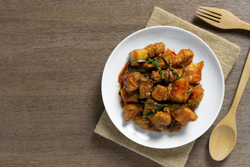 top view of stir fried pork belly with red curry paste in a ceramic dish on wooden table. hot and spicy thai style food menu.
