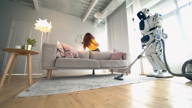 One cyborg uses vacuum cleaner while a woman talks on a phone. Robot and human cooperation.