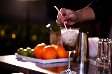 Bartenders hands sprinkling the juice into the cocktail glass filled with alcoholic drink and making a smoky note on the dark background